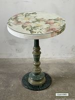 Front view of the small round occasional table showing floral pattern on the glass covered top and marble pedestal base.