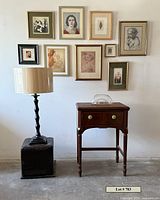 Full view of lamp, sewing table, ottoman, glass bowl on table, and framed artworks on wall