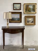 Console table with the lamp on top and four framed paintings hung on the wall behind it.