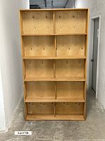 Front view of the large homemade wooden tall shelf showing five levels, each divided into two compartments with visible scratches and imperfections on wood surface.