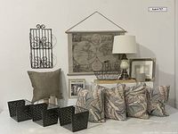 Photo showing tapestry map hanging on wall, lamp with shade on table, stack of metal storage baskets and wire basket, four taupe and teal feather pillows, iron mail holder, new picture frame, and drinking game box.