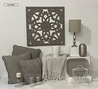 Full grouping of taupe accessories including carved wood wall decor, pillows, vase, lamp, platter, candle holders, and throw blanket arranged for display.