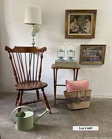 Full view of the lot with Windsor chair, lamp on chair, two framed artworks on wall, two blue lanterns on small folding table, woven basket with coral pillow, and watering can on floor