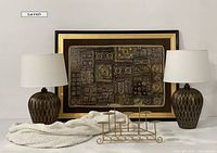 Wide view of the entire lot showing framed embroidered textile, two lamps, candle holder, and throw blanket on floor.