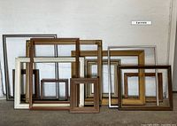 The 12 wooden frames arranged leaning against a wall, showing a mix of large and small sizes and different wood finishes including brown, gold, and white.