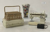 Vintage Kenmore 158.10500 portable sewing machine out of its plastic carrying case with foot pedal and large vase full of spools of thread alongside a wicker sewing basket.