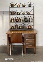 Full front view: desk, chair, metal shelf with 18 watering cans
