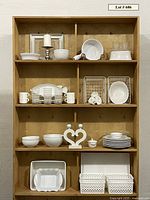 Full shelving unit display of the white serving ware set including bowls, plates, baskets, glassware, and kitchen accessories