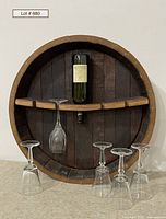 Front view of round wooden wine barrel shelf holding inverted wine bottle and four crystal wine glasses, five glasses total shown with one hanging and four on surface