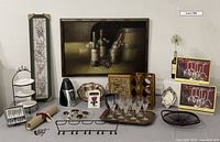 Photo showing the full lot including framed painting, ceramic planter, tiered plate server, wine accessories, silver trays, and books arranged on a table and against a white wall.