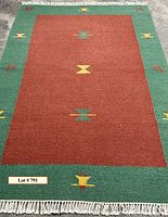 Full view of rectangular rug showing burnt umber central field, green border with yellow and red motifs, cream fringe.