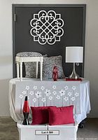 Fabric covered stool, two feather pillows, silver lamp, red sculpture, red and black sparkly lava-type lamp, two red textured pillows, and floral artwork on table; wooden arabesque wall decor mounted on wall above