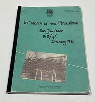 Softcover book with turquoise-green cover, black binding strip, handwritten style text on front, worn edges.