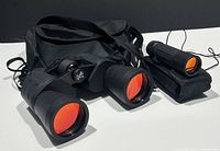 Photo showing black 12x50 binoculars and monocular telescope with orange-red coated lenses next to black carrying case.