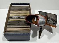 Box of over 140 stereoview cards and handheld stereoscope viewed together
