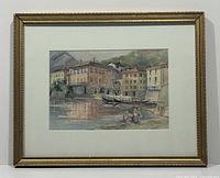 Full image of the framed watercolour painting depicting a waterfront village scene with boats and figures.