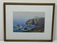 Framed watercolour painting showing coastal cliffs and ocean rocks with signature visible.