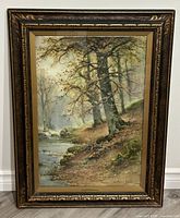 Full view of framed watercolor painting showing forest and stream scene in gold-tone wood frame