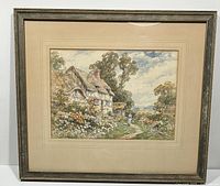 Photo of the entire framed watercolour painting, showing a thatched cottage, garden, and a figure walking on a path under a partly cloudy sky.