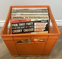 Orange plastic crate filled with 25 vinyl records, visible titles include 'Your Twist Party' by Chubby Checker and 'Original TV Soundtracks'