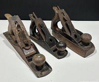 Three vintage wood-bodied hand planes side by side on white background