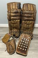 Front view of DR leather vintage goalie pads alongside Copper leather catching glove and blocker on floor
