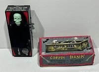 Showing the coffin coin bank next to its original box. The coffin is black with red inside and has a green skeleton visible under plastic.