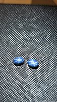 Pair of blue 6-ray star sapphires on textured black background showing clear asterism effect.