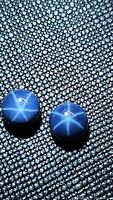 Pair of round cabochon blue star sapphires on textured black surface showing six-ray star effect.