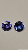 Pair of round deep purple blue tanzanite gemstones on neutral background, close-up showing cut and clarity