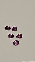Five oval faceted rubies in pink, purple and red colors on a light background.
