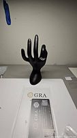 Men's ring displayed on black hand mannequin with GRA certification card visible below.
