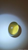 Yellow translucent oval cabochon citrine gemstone viewed from top under direct light, showing clarity and rounded dome shape.