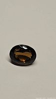 Single deep cognac colored oval cut gemstone shown on plain background, details of facets visible