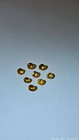 Photo of nine natural round cut yellow sapphires spread on a light background showing color and shape.