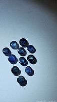 Top view of 11 natural blue sapphire round cabochon gemstones arranged on a surface under lighting highlighting color and translucency