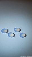 Four oval cabochon chalcedony stones white to lavender color translucent set on white background.