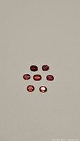 Seven natural faceted orange sapphire and ruby gemstones arranged in a cluster on a flat surface.