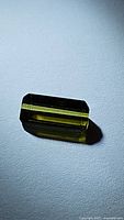 Close-up photo of a rectangular bright green tourmaline gemstone with step-cut facets on a light surface.