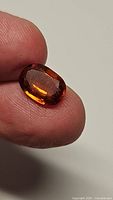 Close-up of oval faceted hessonite garnet held between fingers showing deep orange color and facets.