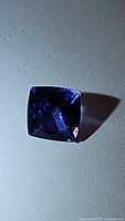 Close-up image showing the cushion cut natural tanzanite gemstone with its rich purple-blue color and faceted surface reflecting light.
