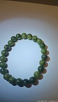 Full view of the natural green jade chunky bead bracelet laid flat on a surface showing bead color, size, and round shape.