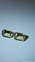 Photo of two natural lemon citrine emerald cut gemstones placed on a flat surface showing color and cut details.