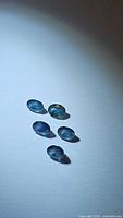 Five oval cut natural blue-green sapphires arranged and photographed to show color and shape.