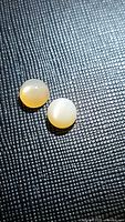 Two round polished peach moonstone cabochon gemstones on black textured background, showing translucency and cat's eye flash.