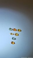 Top view of eight small pear cut sapphires in green, yellow and orange hues arranged on a plain background.
