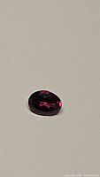 Oval cut natural rhodolite garnet gemstone with hot pink color, faceted, placed on a neutral background