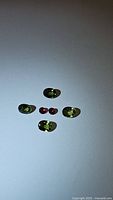 Five green sapphire gemstones in oval and round cuts along with two deep red ruby gemstones placed on white background.