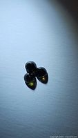 Photo of three dark green round faceted gemstones on plain white background, showing their shape and color.