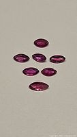Seven marquise cut pink-red natural untreated rubies arranged in two rows on a light background.
